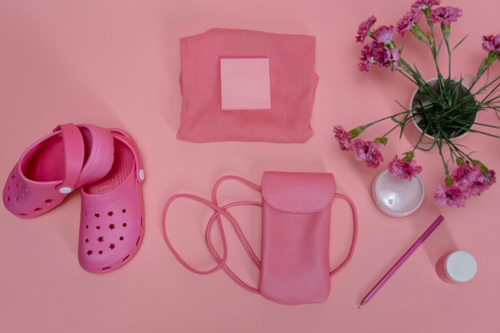Flat lay of pink items including crocs, bag, flowers on a pastel surface.
